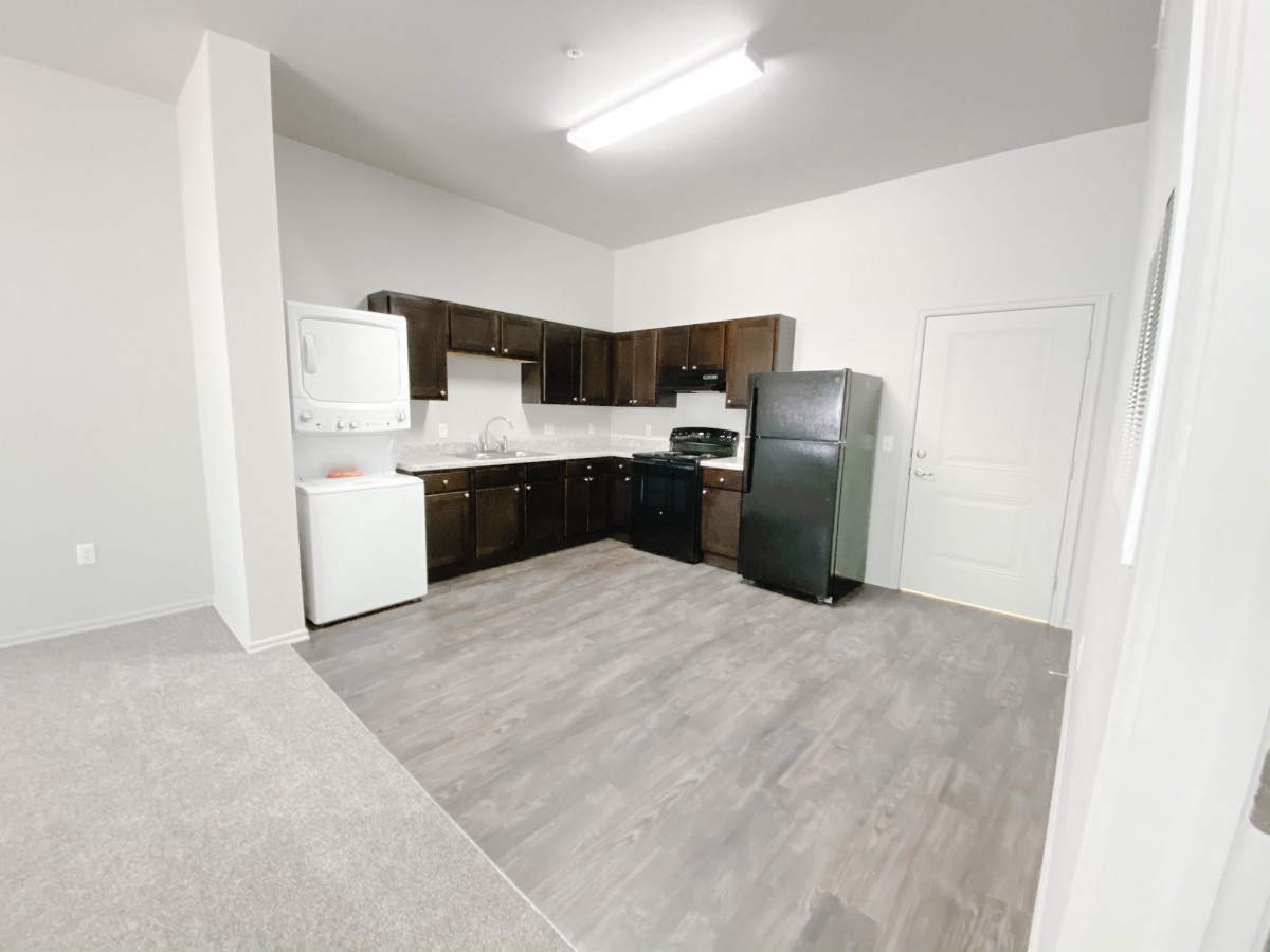 A modern apartment kitchen with dark cabinets and light flooring.