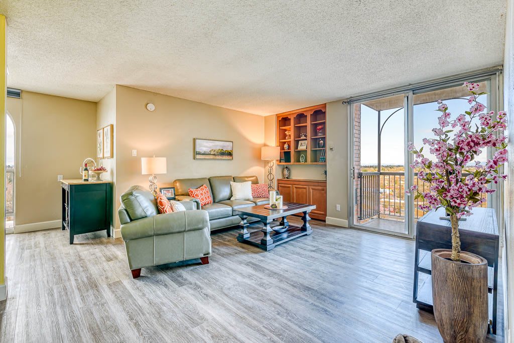 A cozy living room with modern furnishings, featuring a comfortable sofa, coffee table, and built-in bookshelves. Large windows allow plenty of natural light to fill the space.