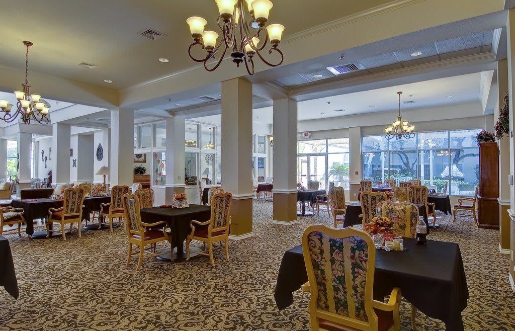 A spacious dining area with elegant chandeliers, tables, and chairs set on a carpeted floor.