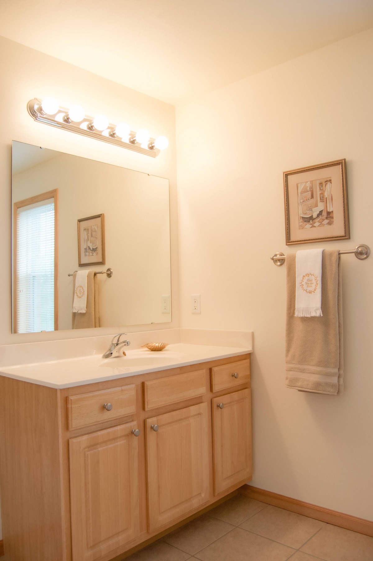 A clean and simple bathroom with a large mirror, wooden cabinets, and a towel rack.