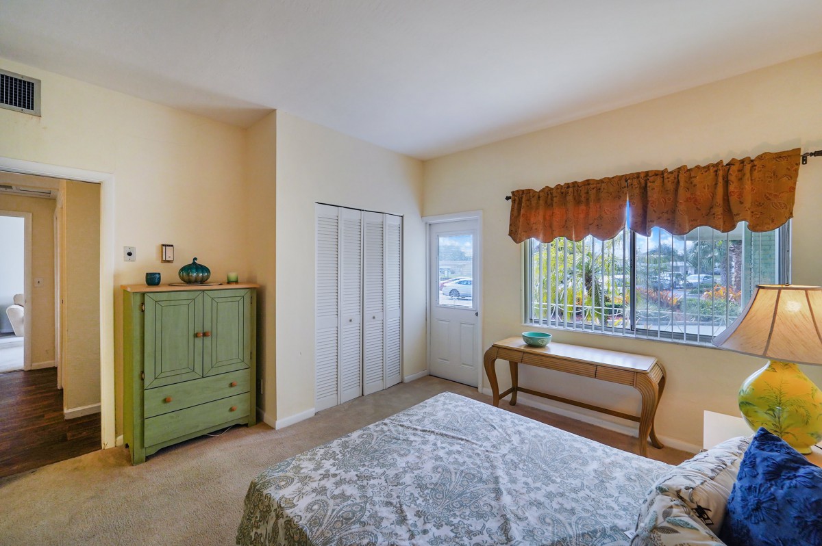 A cozy bedroom with a window allowing natural light, featuring a green dresser and a bed with a patterned bedspread.