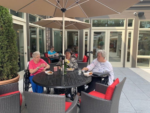 Seniors enjoying a pleasant day outdoors, sharing food and conversation under an umbrella.