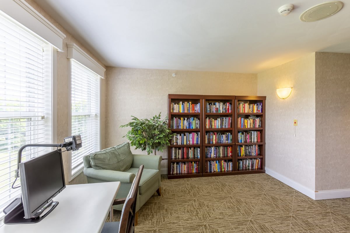A cozy library corner with bookshelves, a comfortable chair, and a computer desk by the window.
