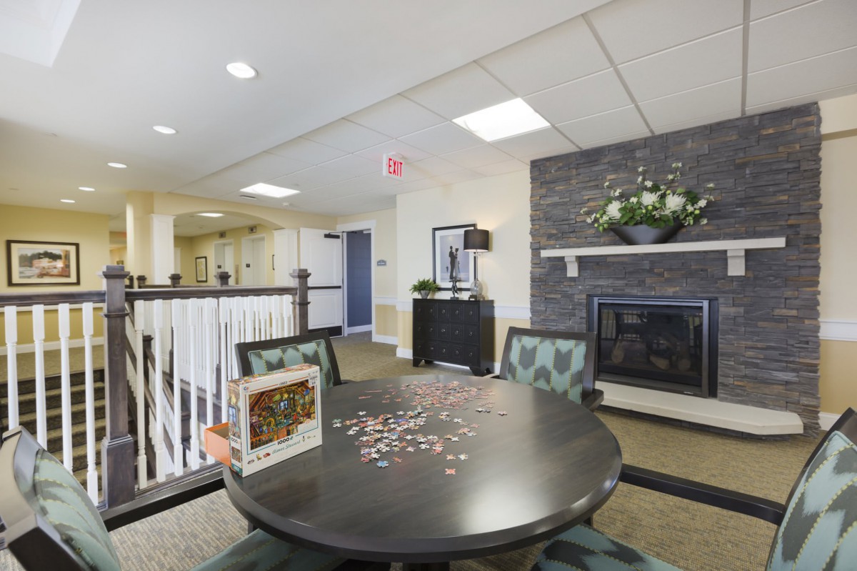 A cozy living room with a fireplace, round table, and chairs, featuring a partially completed puzzle on the table.