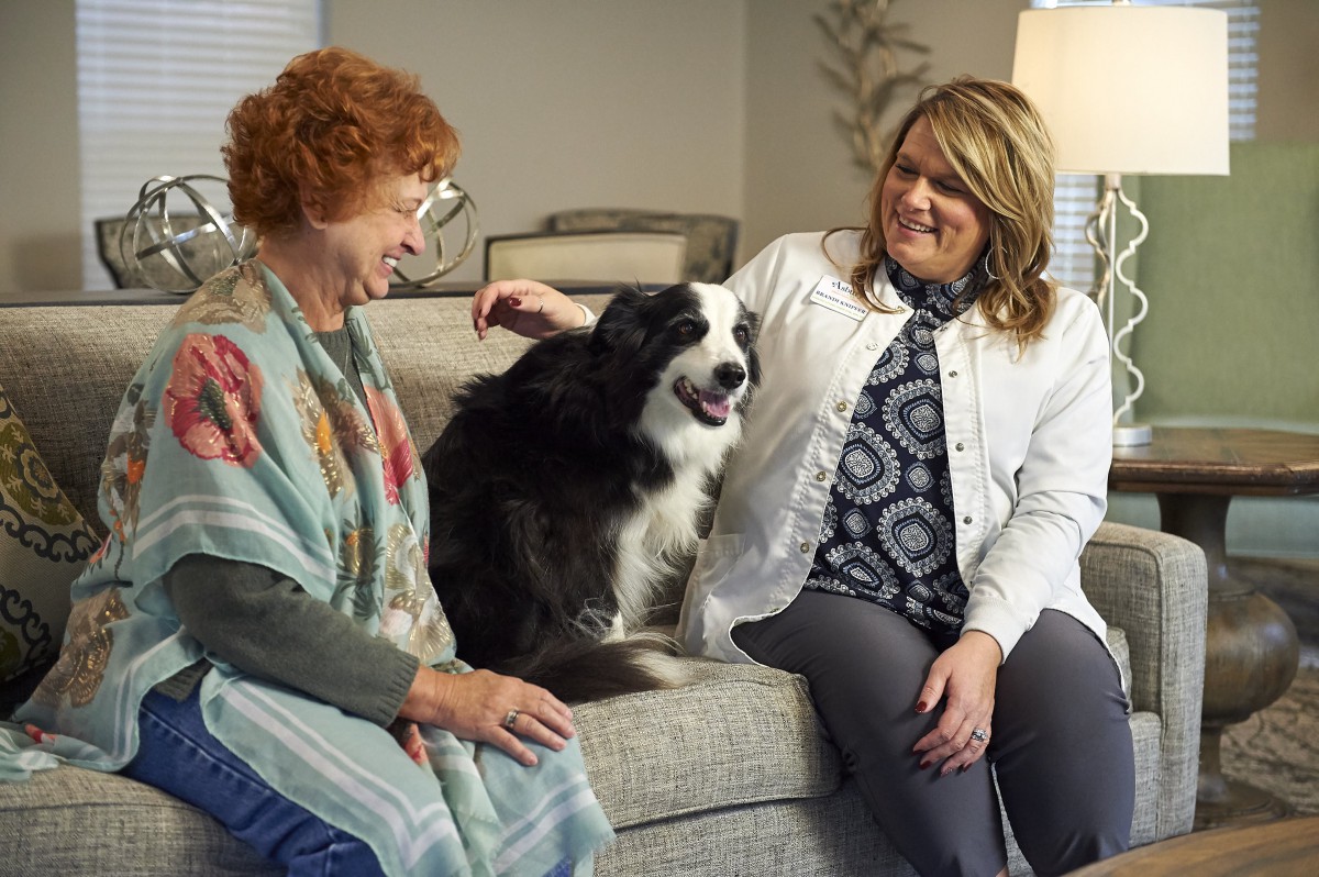 Two people sitting on a couch with a dog, enjoying their time together in a living room.