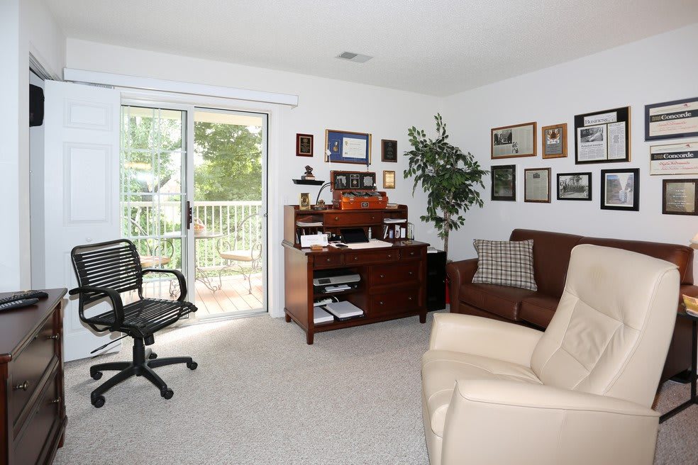 A cozy home office with a desk, chair, and sofa in a well-lit room.