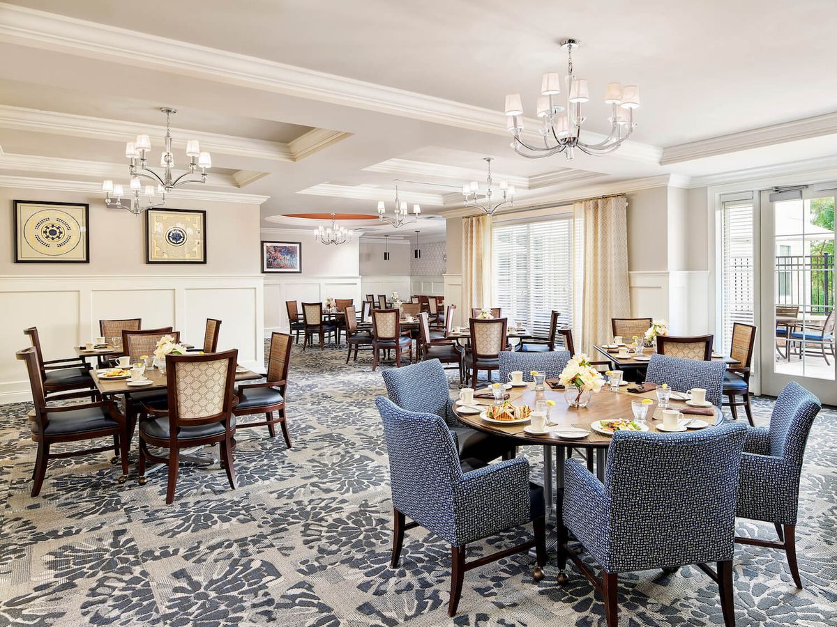 An elegant dining room with beautifully set tables, featuring chandeliers and a carpeted floor.