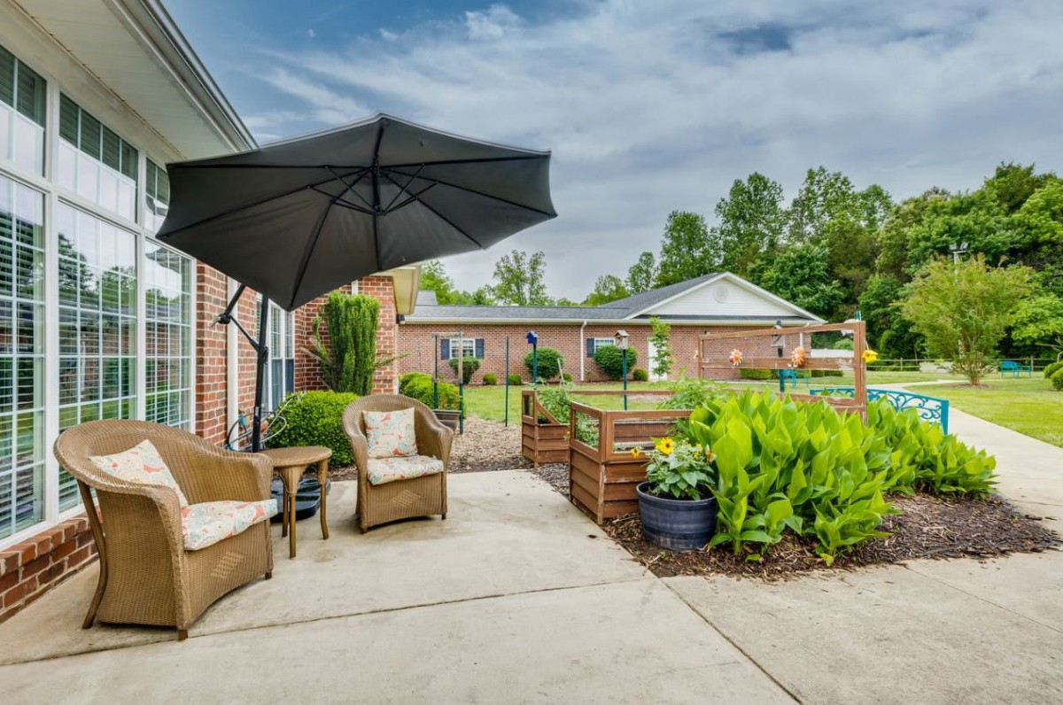 A cozy patio area with comfortable seating and a large umbrella, surrounded by lush greenery.