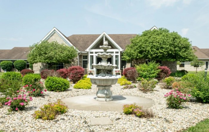 A beautiful garden with a central fountain in front of a house.