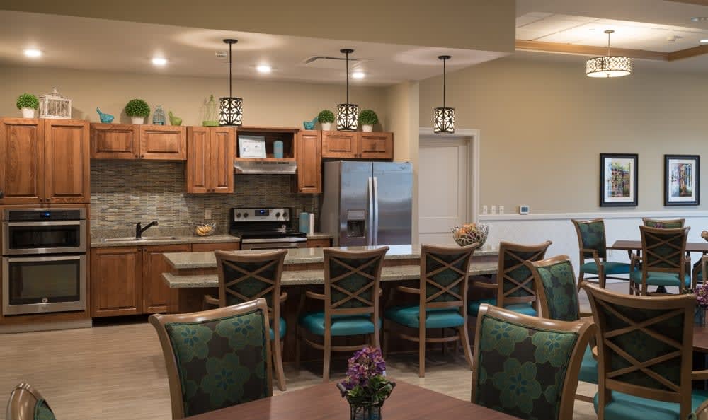 A modern kitchen and dining area featuring wood cabinets, stainless steel appliances, bar stools, and pendant lights.