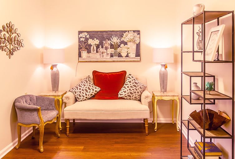 A cozy living room setup with a white sofa adorned with patterned and red cushions, flanked by elegant lamps and artwork on the wall.