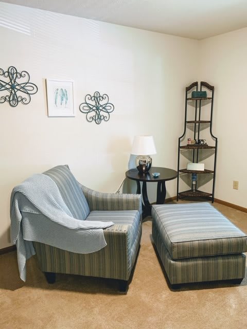 Cozy living room corner with a striped chair and ottoman, complemented by decorative wall art and a side table lamp.
