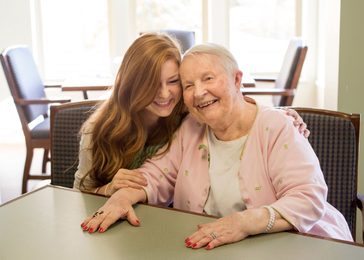A young woman and an elderly woman share a warm, happy moment together.