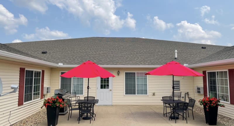 Outdoor patio area with tables, chairs, and red umbrellas in front of a building.