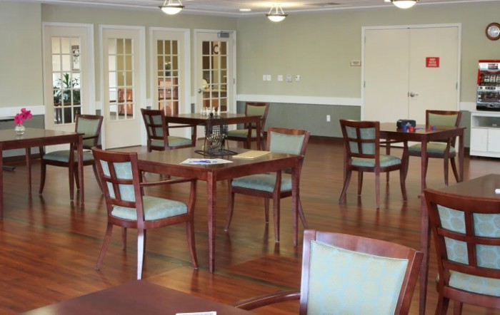 A spacious dining area with several wooden tables and chairs arranged neatly, set on a polished hardwood floor.