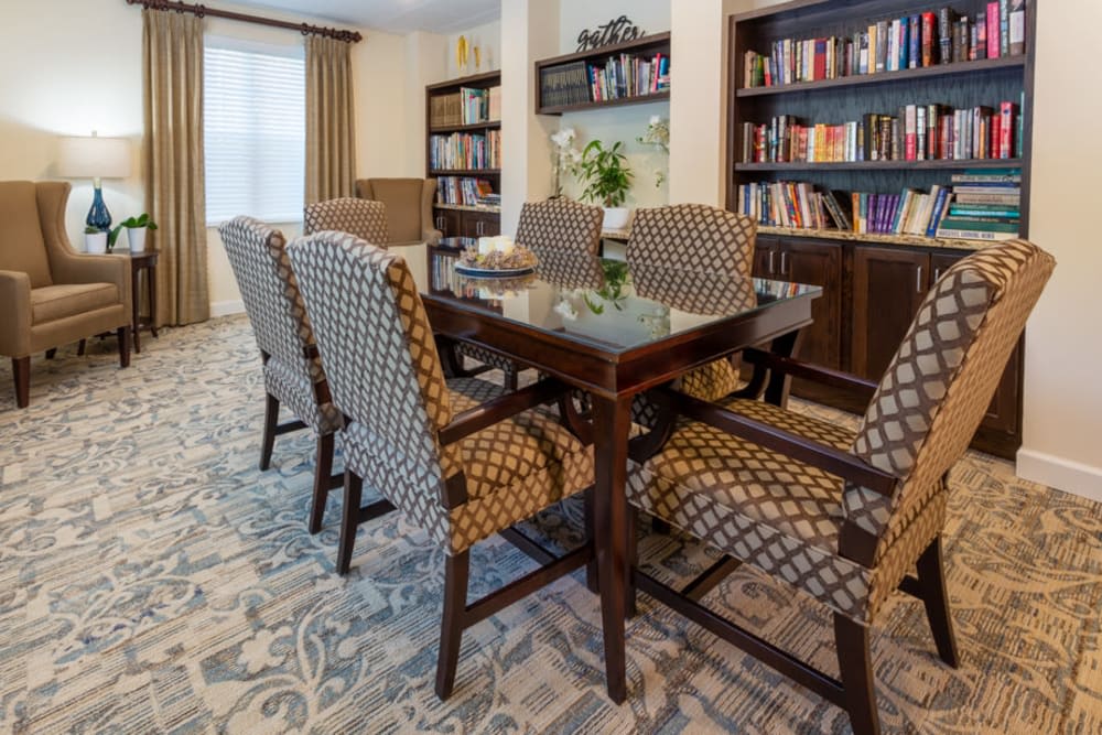 A dining area with a table and patterned chairs, surrounded by bookshelves and a carpeted floor.