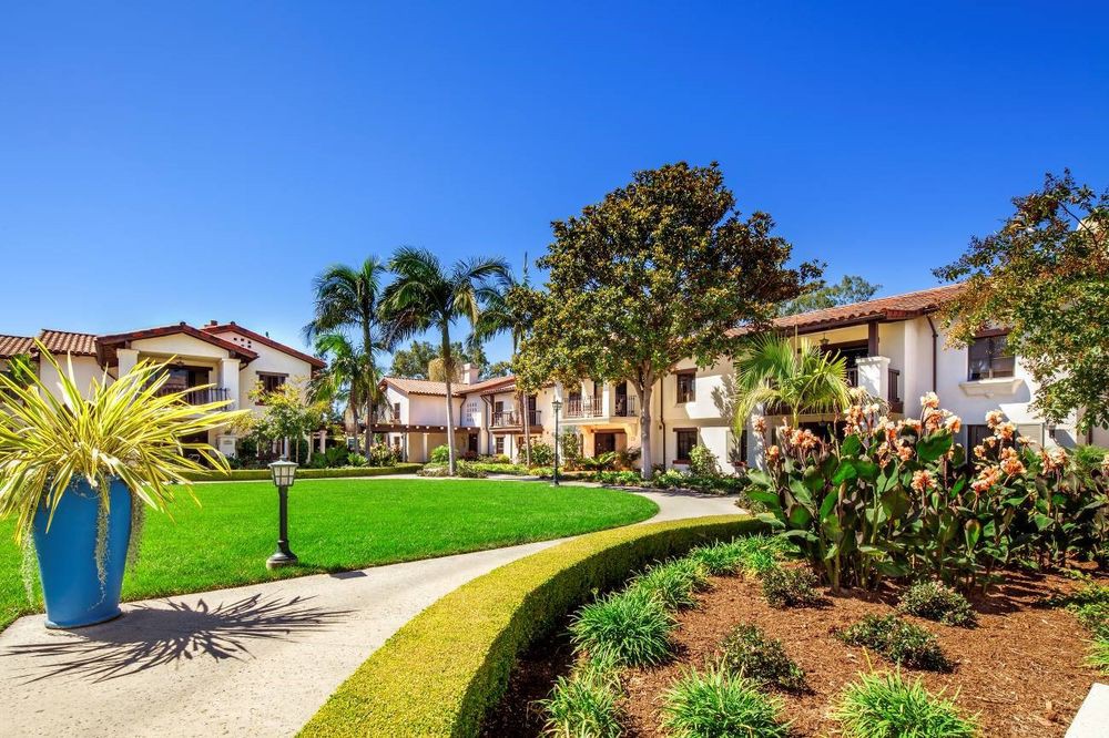 A landscaped residential area with a pathway, greenery, and palm trees under a clear blue sky.