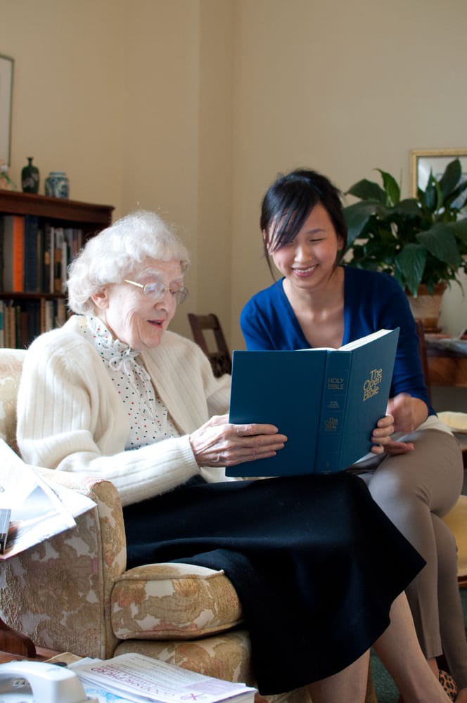 An elderly woman reading a book with the assistance of a younger woman.