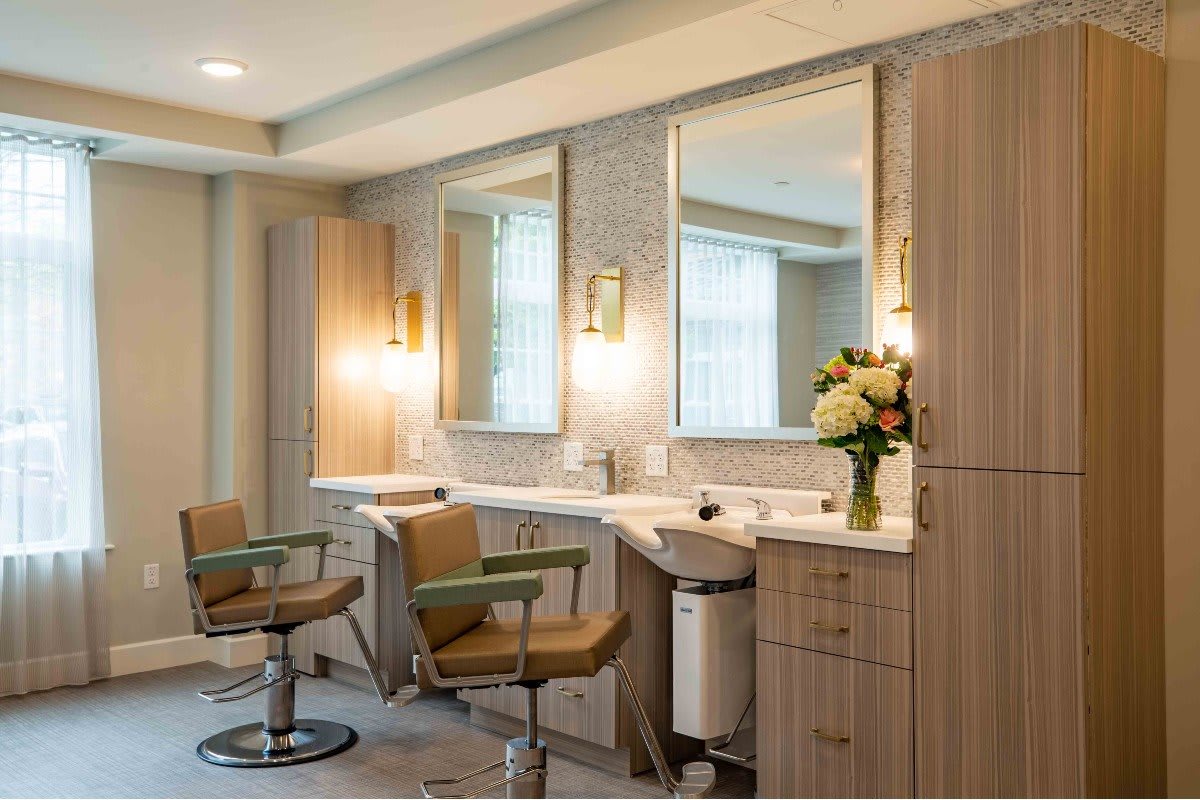 A modern salon interior with stylish chairs and mirrors, complemented by warm lighting and a bouquet of flowers.