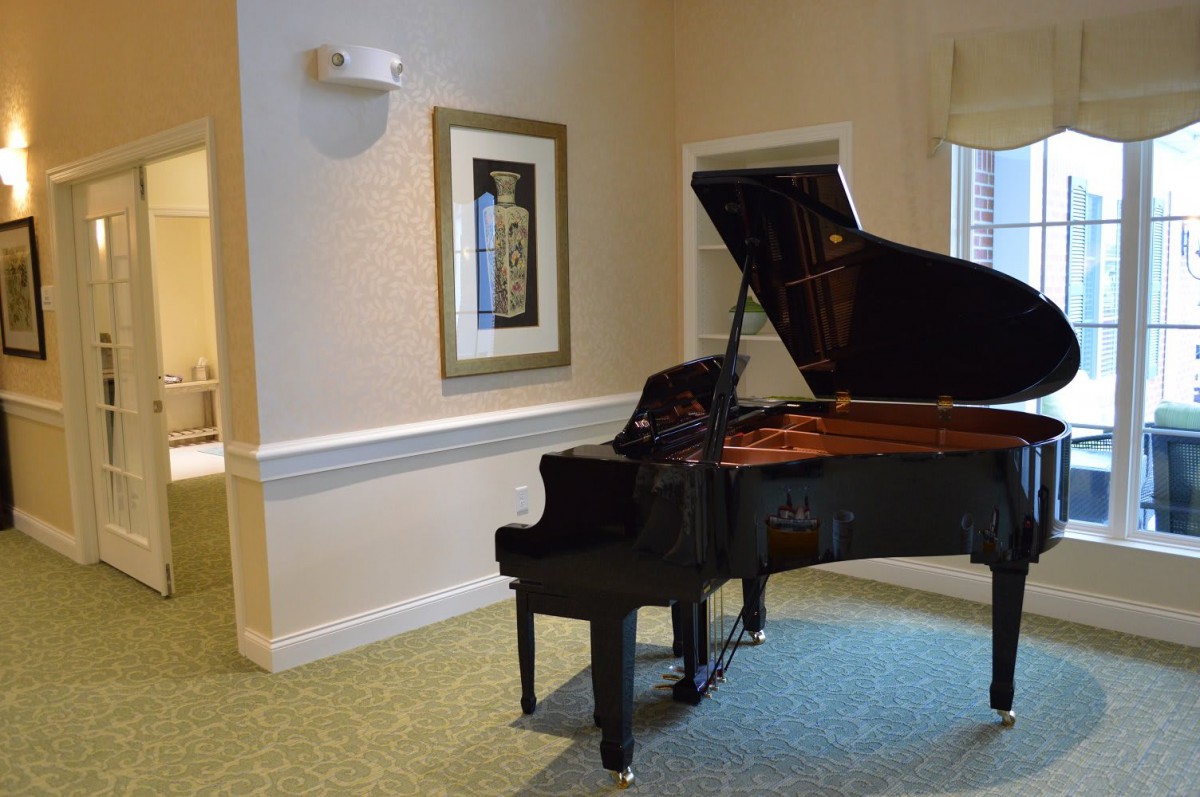 A grand piano in a well-lit interior room with artwork on the wall.