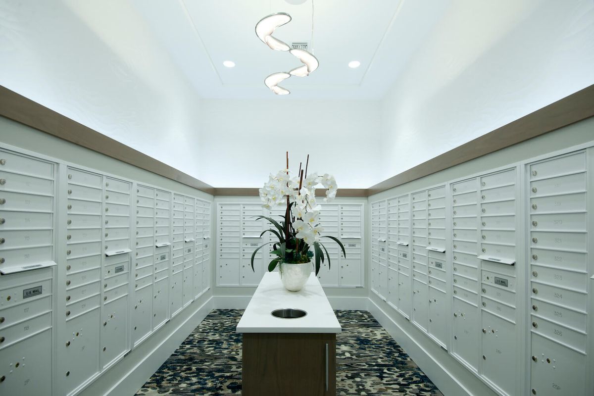 A modern mailroom with white lockers and a decorative flower arrangement.