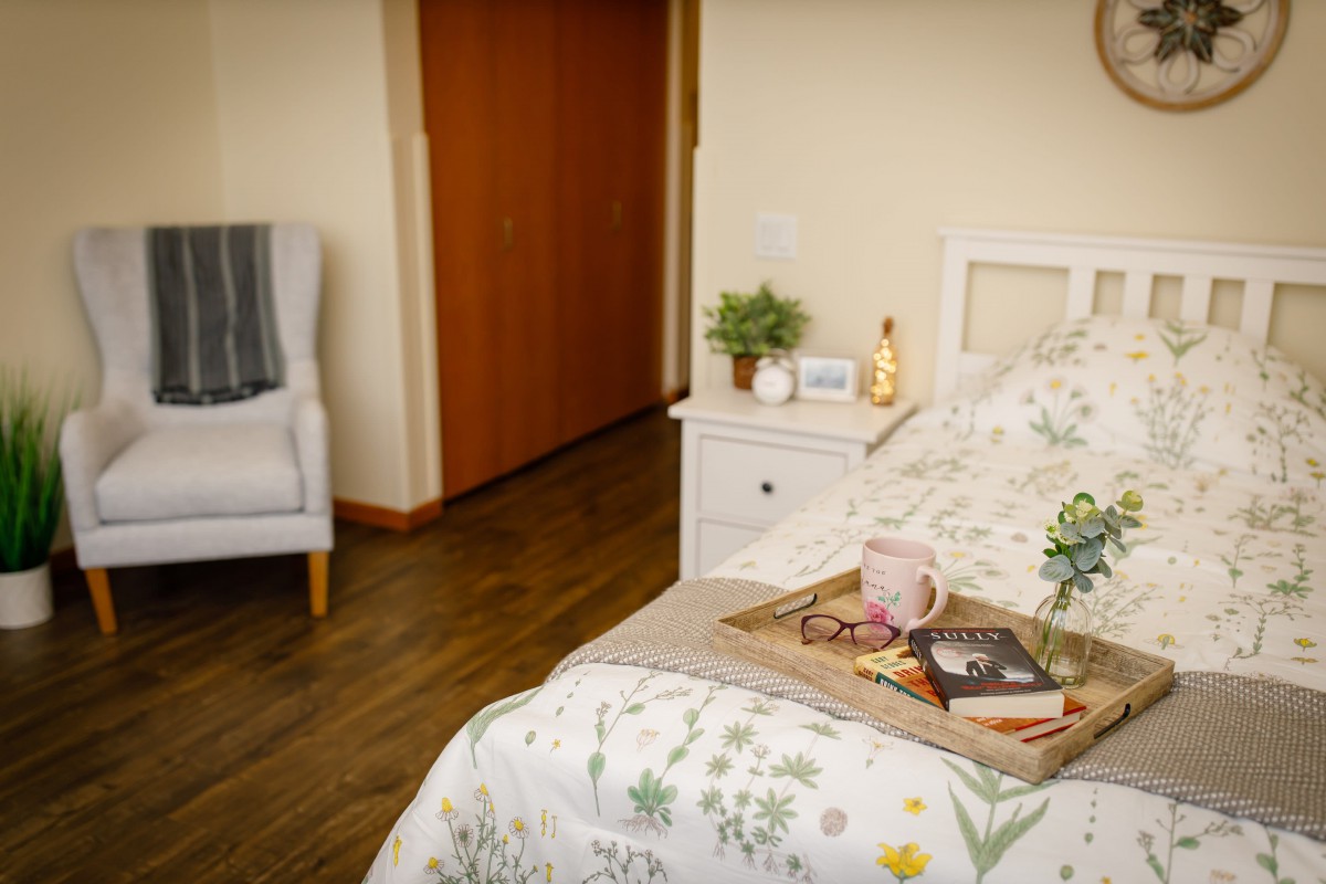 A cozy bedroom setup with a breakfast tray on the bed, featuring a comfortable armchair and wooden flooring.
