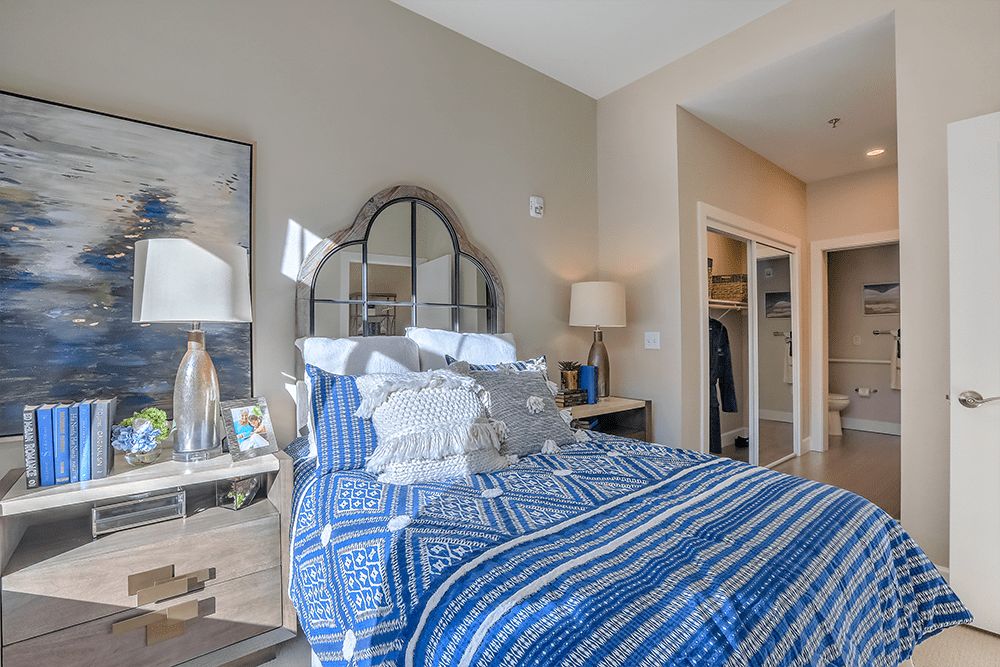 A cozy bedroom with blue bedding, decorative pillows, and a stylish mirror above the bed.