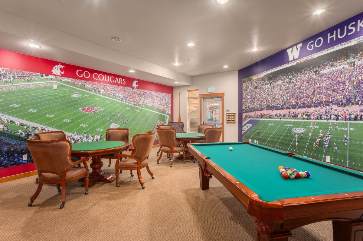 A sports-themed game room featuring a billiards table and seating area with wall murals depicting football fields.