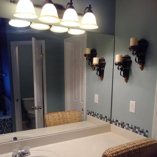 A bathroom featuring a large mirror, overhead and sconce lighting, with a sink and decorative tile border.