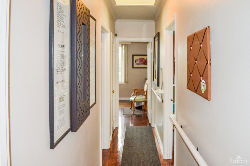 A well-lit hallway with artwork and a wooden floor, leading to a room.