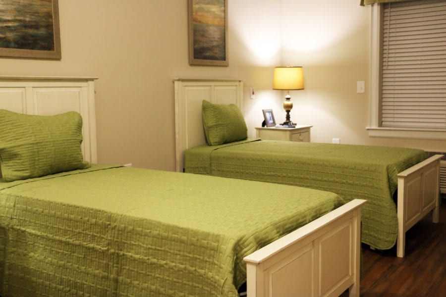 A cozy bedroom with twin beds featuring green bedding, accompanied by a nightstand and lamp.