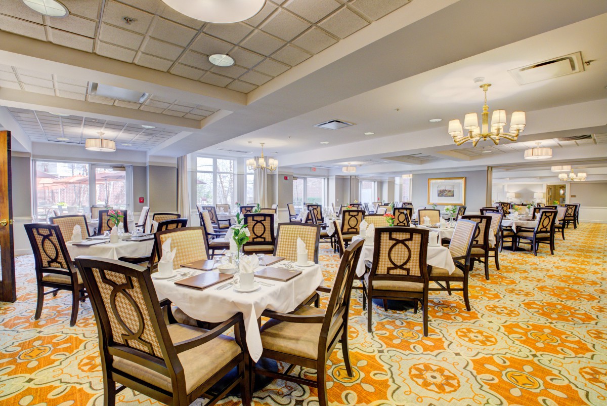 An elegant dining room with neatly arranged tables and chairs, featuring chandeliers and decorative carpeting.