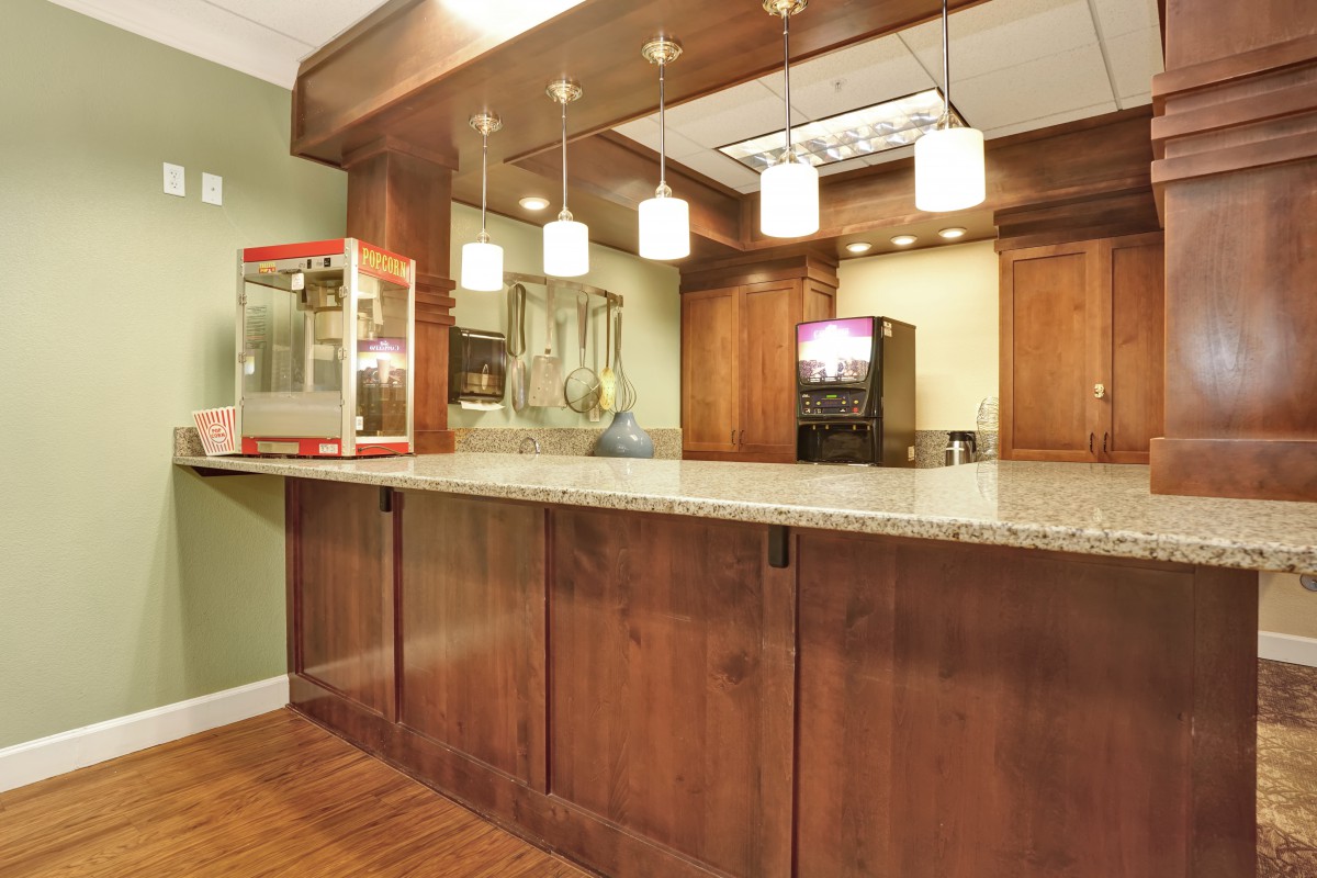 A cozy home bar setup featuring wooden cabinetry, pendant lighting, a granite countertop, and a popcorn machine.