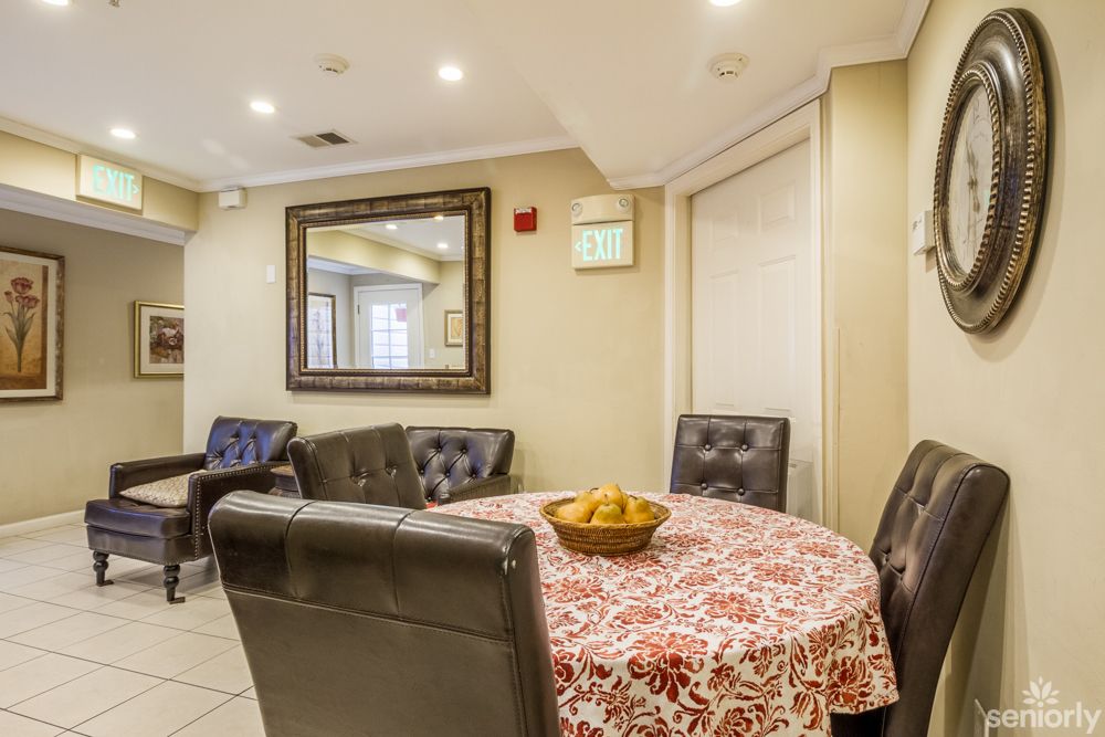 A cozy dining area with a round table covered by a patterned tablecloth, surrounded by leather chairs, and adorned with a decorative mirror on the wall.