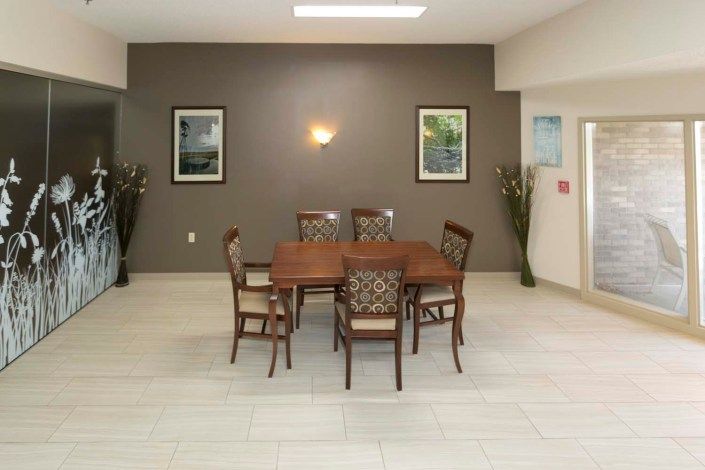 A neatly arranged dining room with a wooden table, six chairs, artwork on the walls, and ambient lighting.