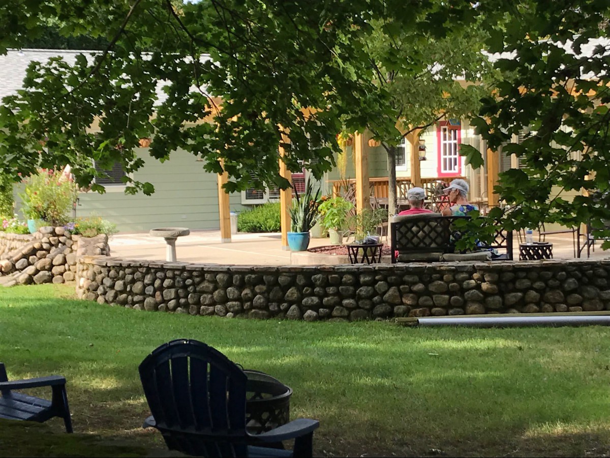 A cozy outdoor patio with a stone wall surrounded by greenery.