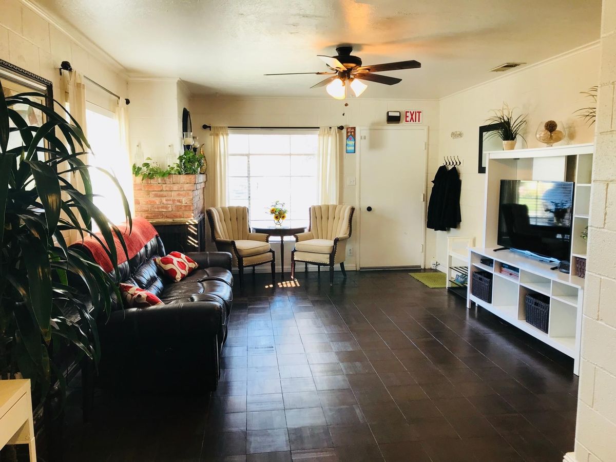 A cozy living room with modern furnishings, including a sofa, TV, plants, and a small dining area.