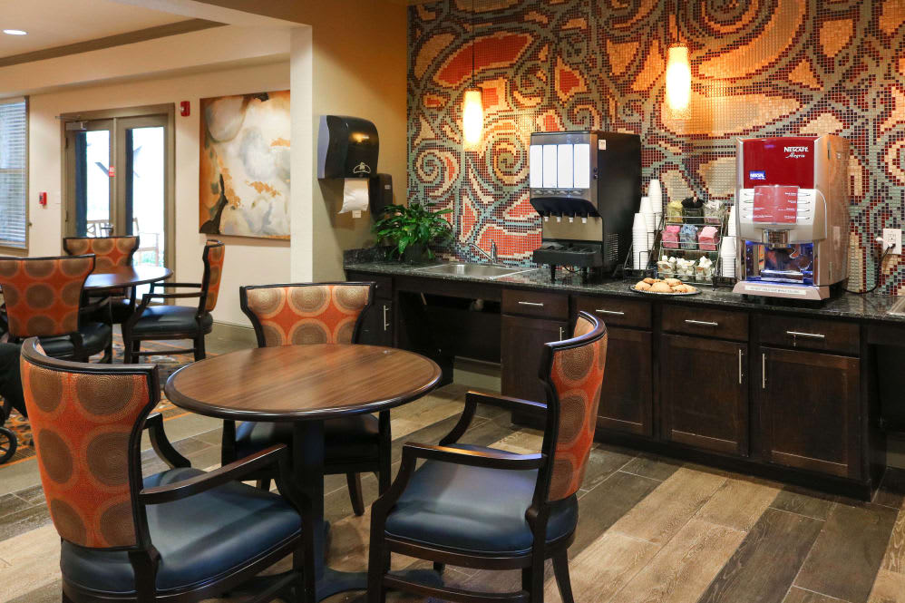 A cozy hotel lobby featuring a coffee station and seating area with modern furnishings and artistic wall decor.