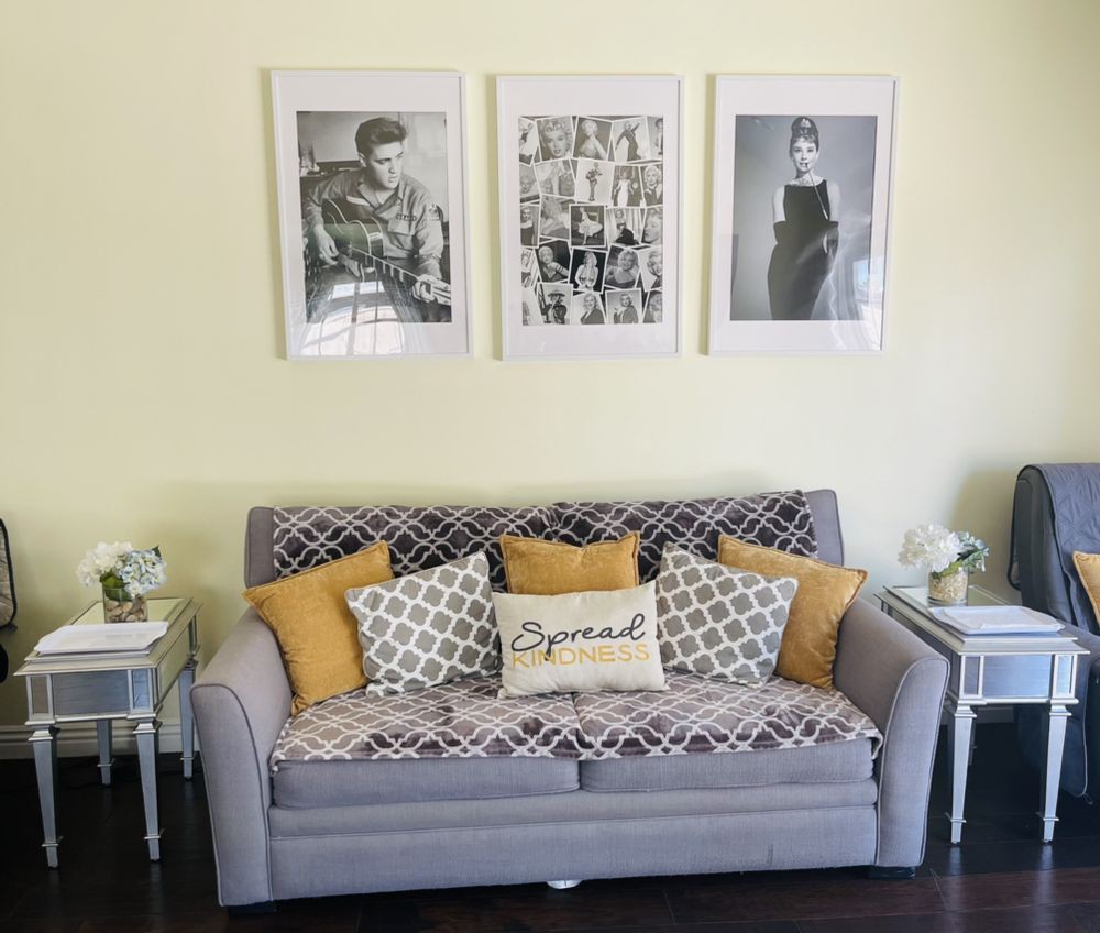 A modern living room with a stylish grey sofa, adorned with patterned and yellow accent pillows, and three framed artworks on the wall.