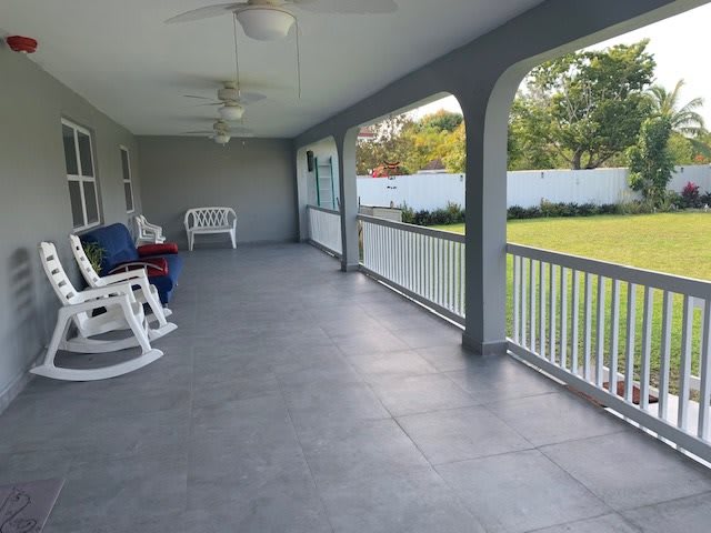 A spacious covered porch with rocking chairs overlooks a green lawn.