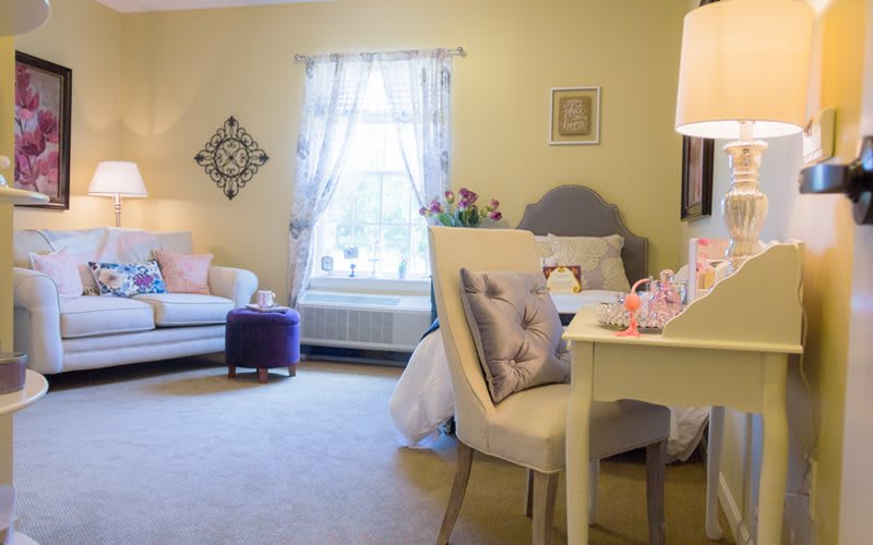 A cozy bedroom with elegant decor, featuring a bed, chair, and sofa with decorative pillows.