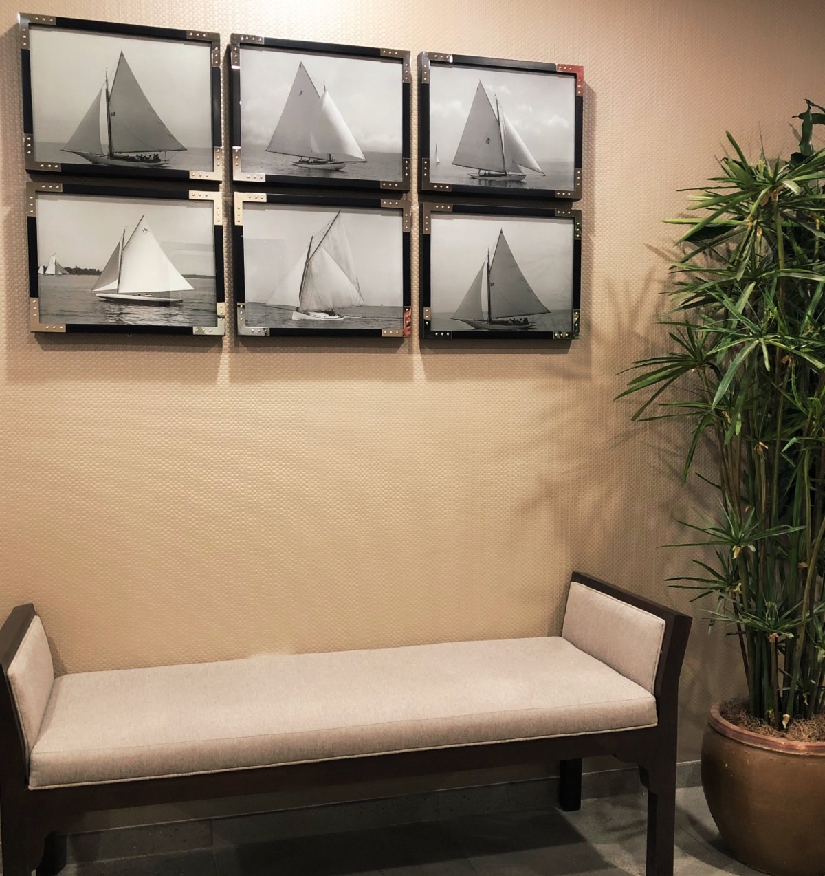 A cozy interior featuring a bench, artwork of sailboats, and a potted plant.