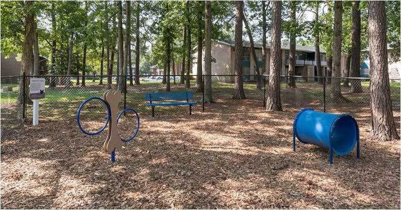 An outdoor exercise area with fitness equipment and benches surrounded by trees.