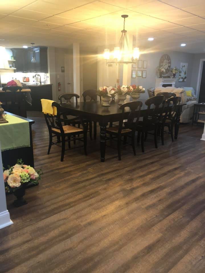 A cozy dining area with a large table, surrounded by chairs and warm lighting, featuring wood flooring.