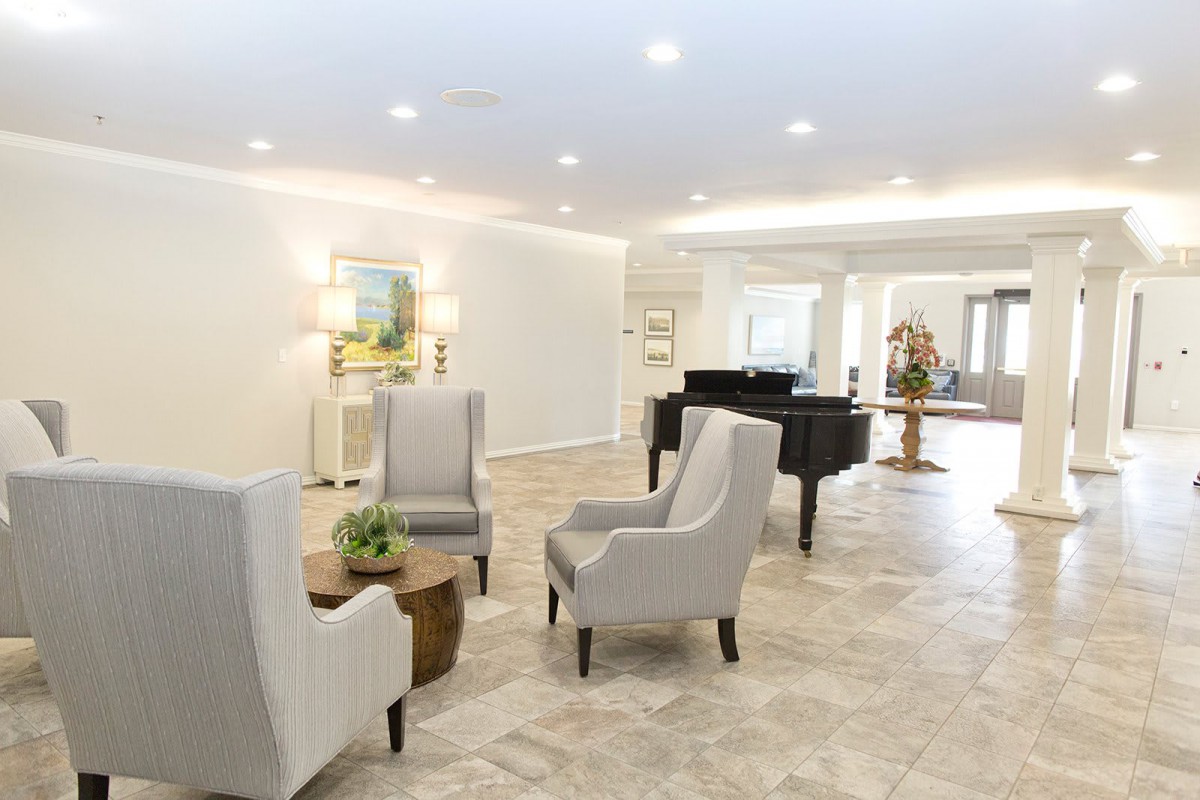 A spacious modern living room featuring a grand piano, elegant armchairs, and minimalist decor with soft lighting.