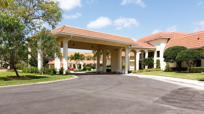 Entrance of a building with a covered driveway and landscaped surroundings.