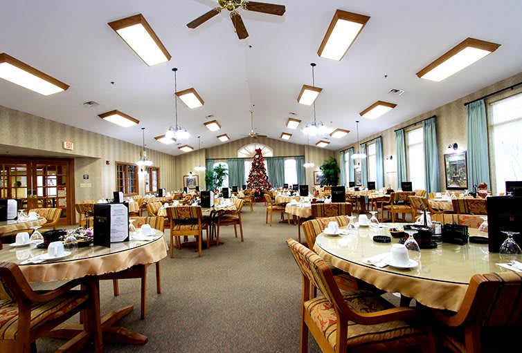 A well-lit dining room with arranged tables and chairs, featuring a decorated ceiling with fans and lights.
