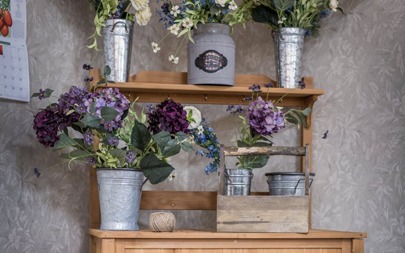 A rustic wooden shelf adorned with potted flowers and vintage-style containers.