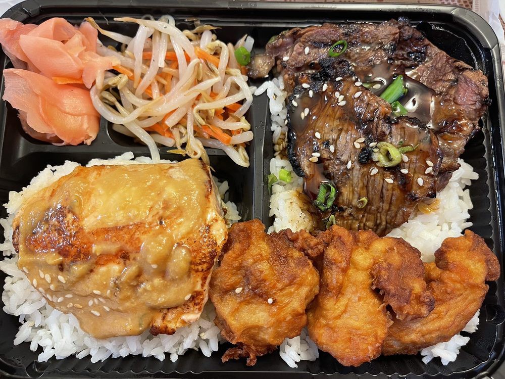 A bento box with grilled meat, fried chicken, tofu, pickled vegetables, and rice.