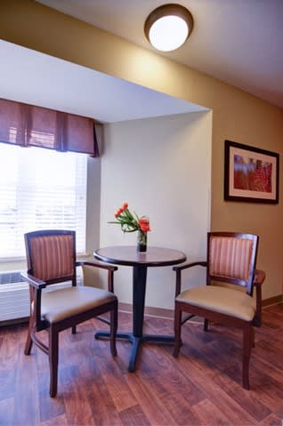 A cozy corner featuring a small table with two chairs, adorned with a vase of flowers and a painting on the wall.